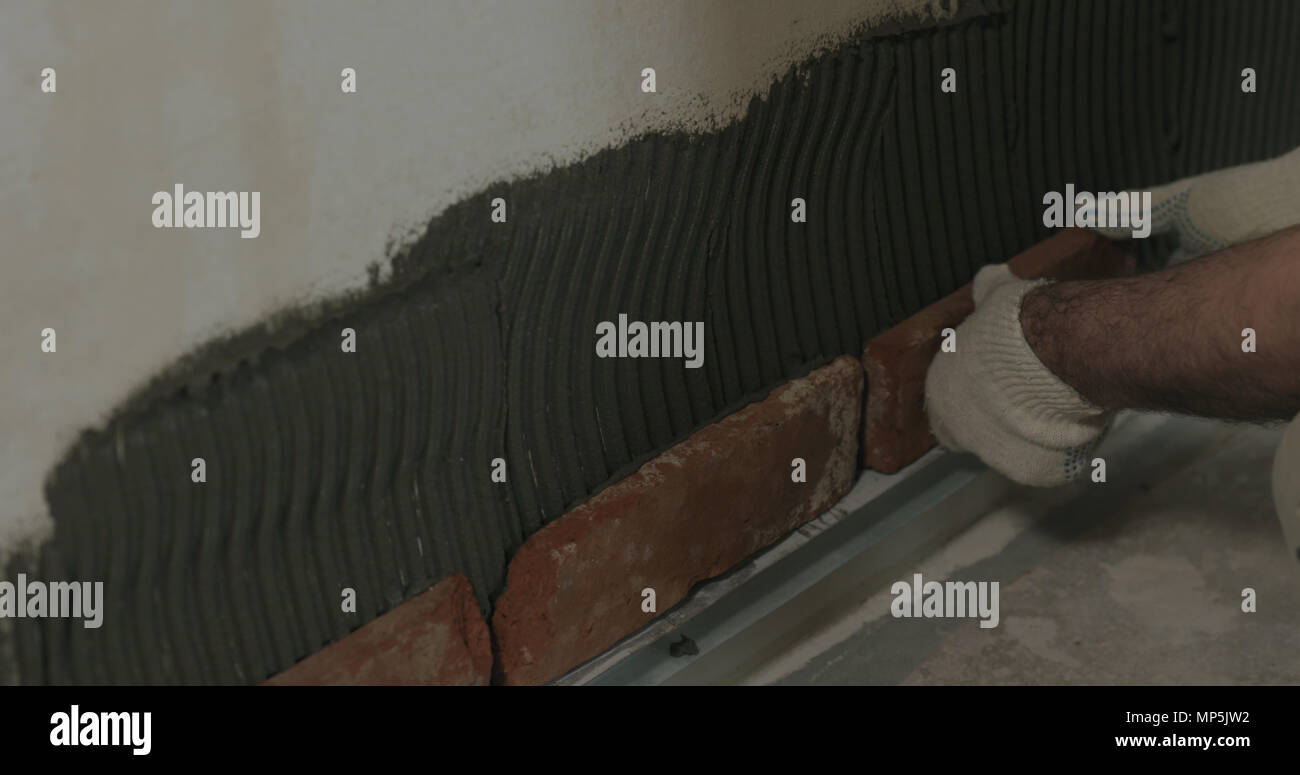 closeup worker applying brick cuts tile on the wall Stock Photo