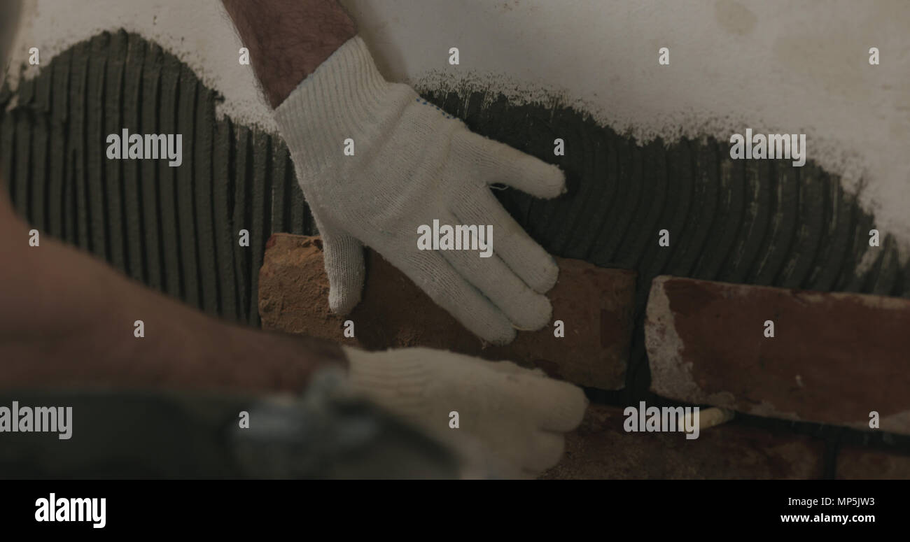 closeup worker applying brick cuts tile on the wall Stock Photo