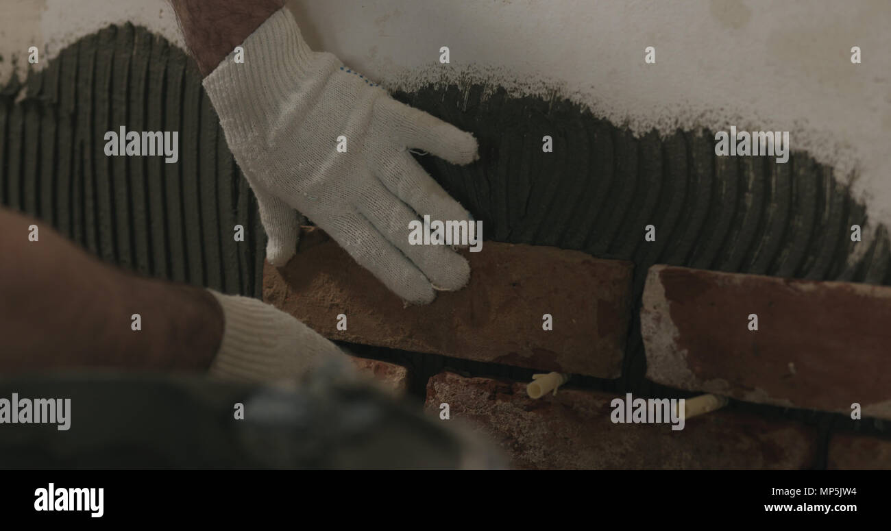 closeup worker applying brick cuts tile on the wall Stock Photo