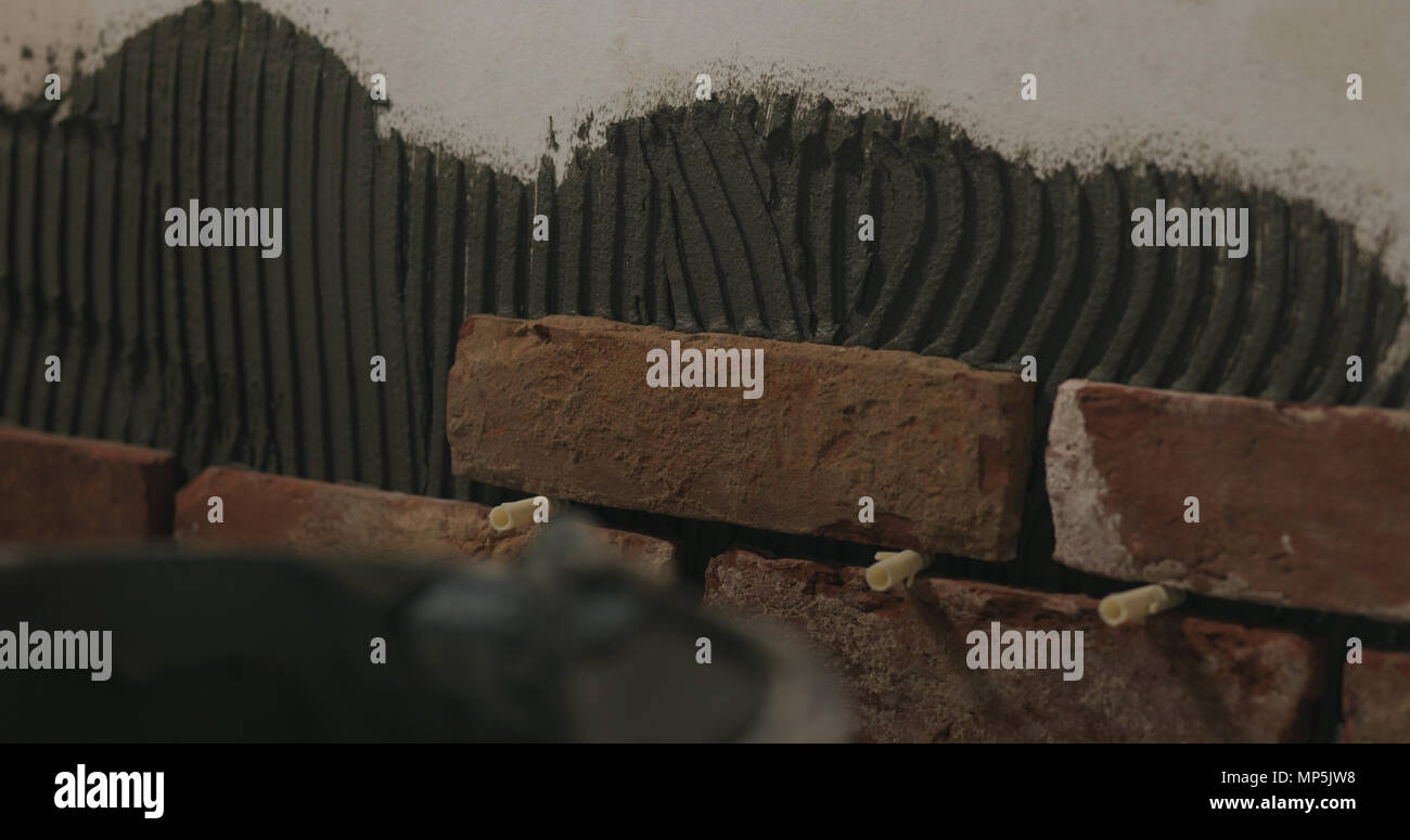 closeup worker applying brick cuts tile on the wall Stock Photo