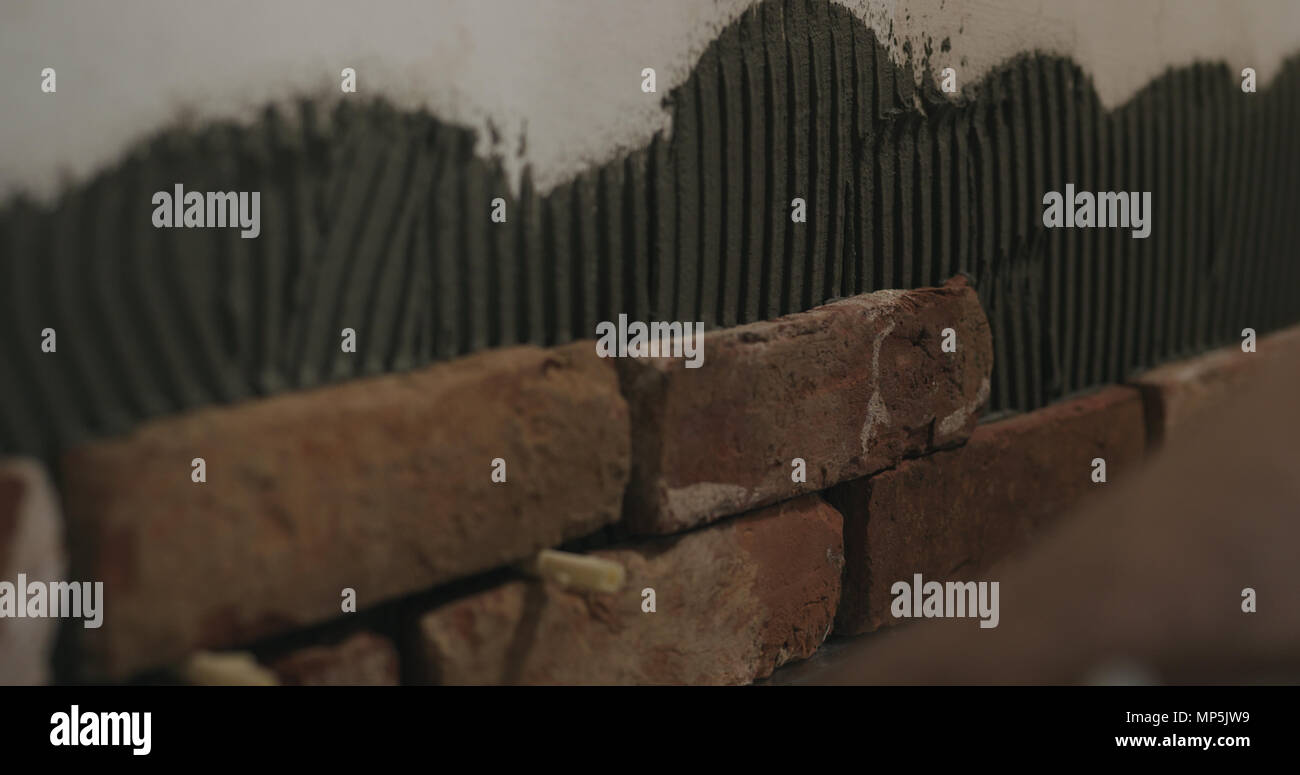 closeup worker applying brick cuts tile on the wall Stock Photo