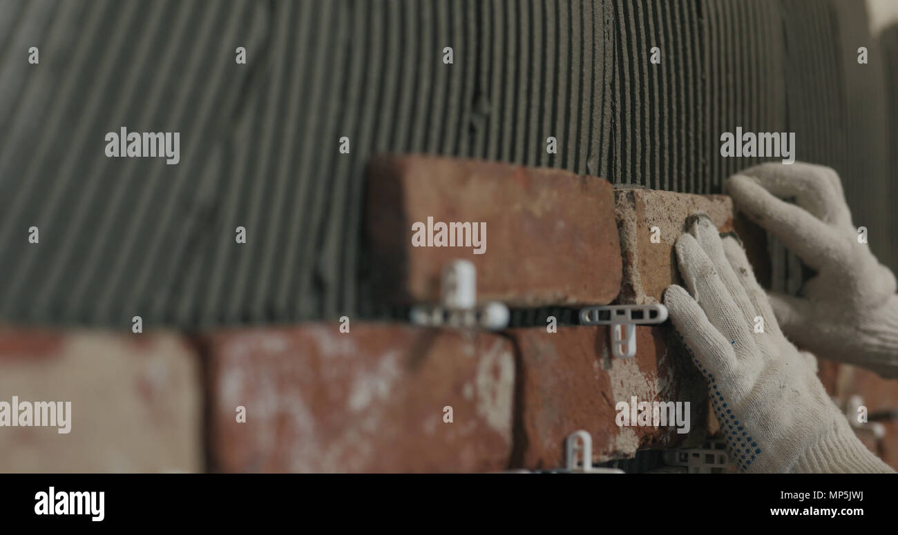 closeup worker applying brick cuts tile on the wall Stock Photo