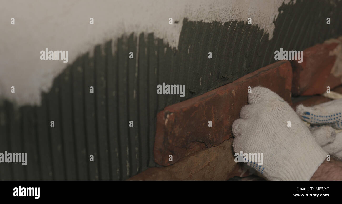 closeup worker applying brick cuts tile on the wall Stock Photo