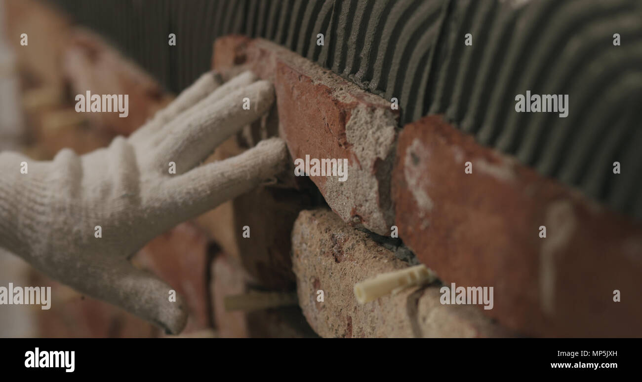 closeup worker applying brick cuts tile on the wall Stock Photo