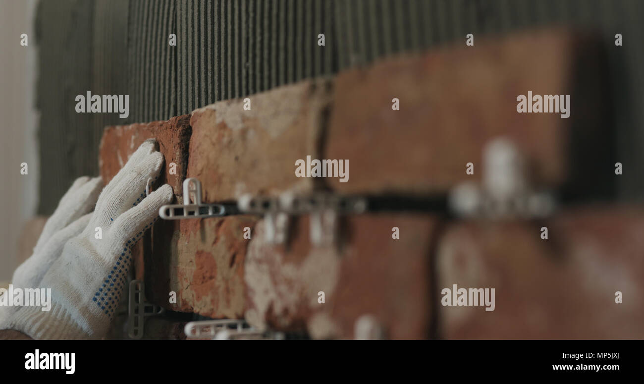 closeup worker applying brick cuts tile on the wall Stock Photo