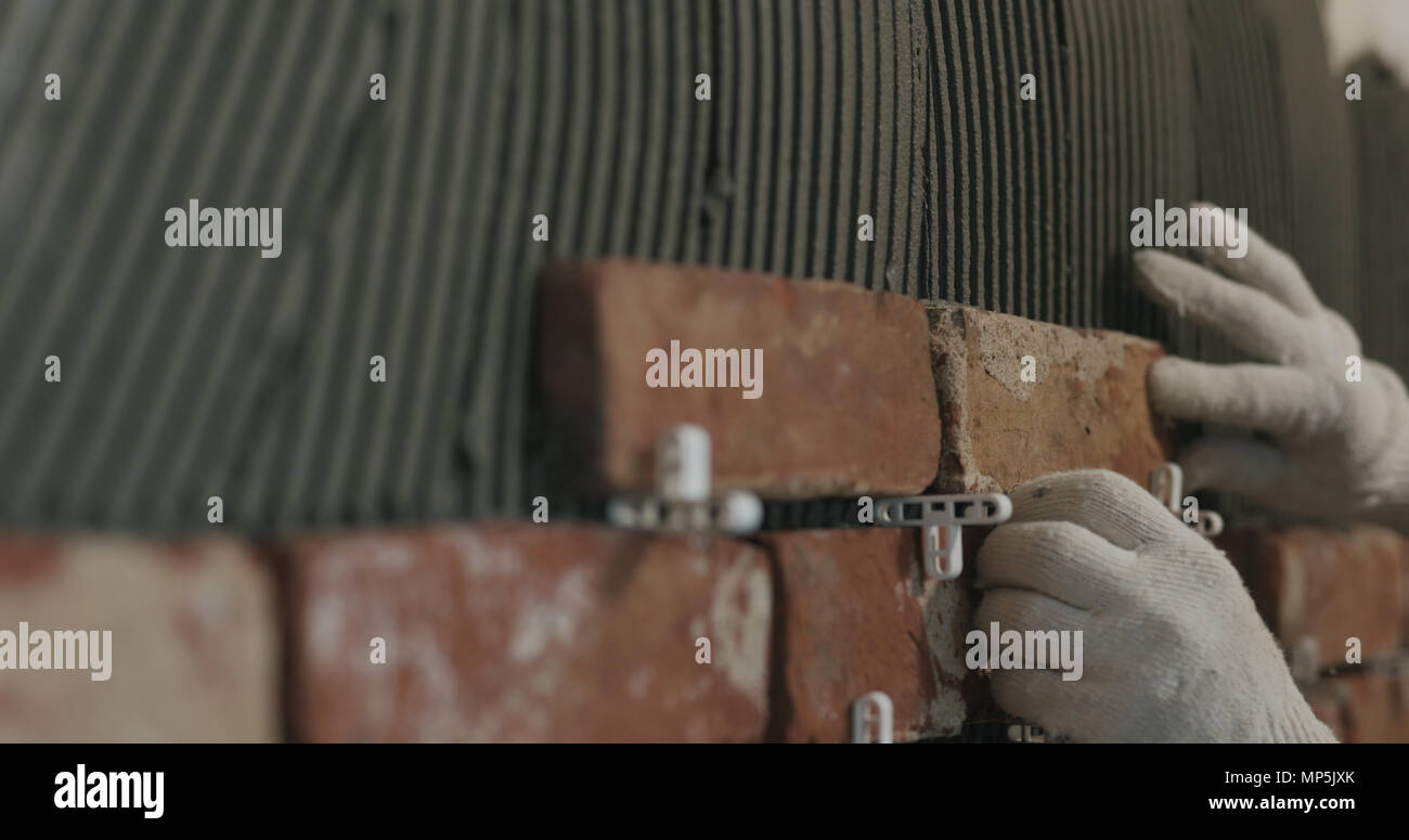 closeup worker applying brick cuts tile on the wall Stock Photo