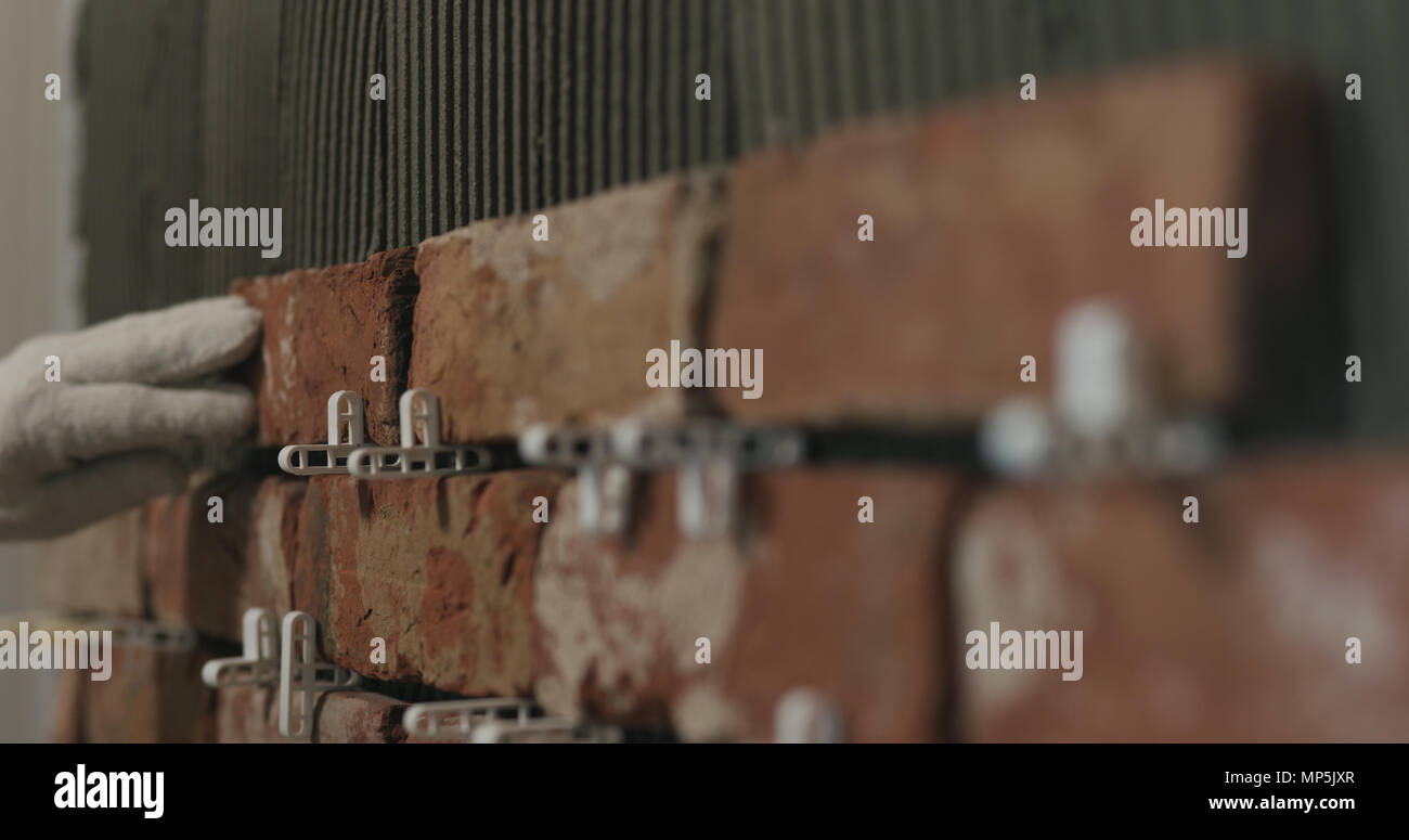closeup worker applying brick cuts tile on the wall Stock Photo