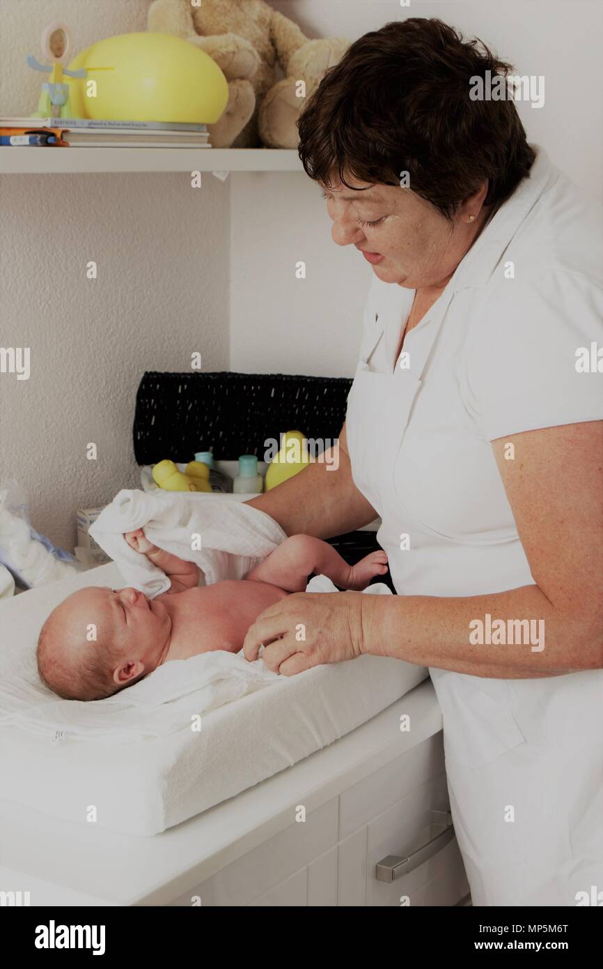 Dutch maternity nurse dressing up newborn baby, assisting the new mother as part of Dutch Kraamzorg. Stock Photo