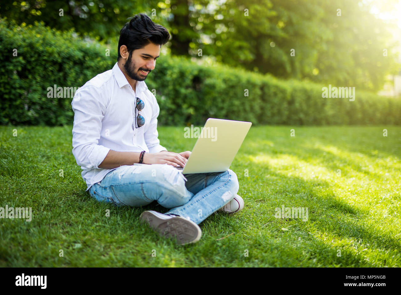 Young indian Student with a laptop sitting on the grass. Urban style. Stock Photo