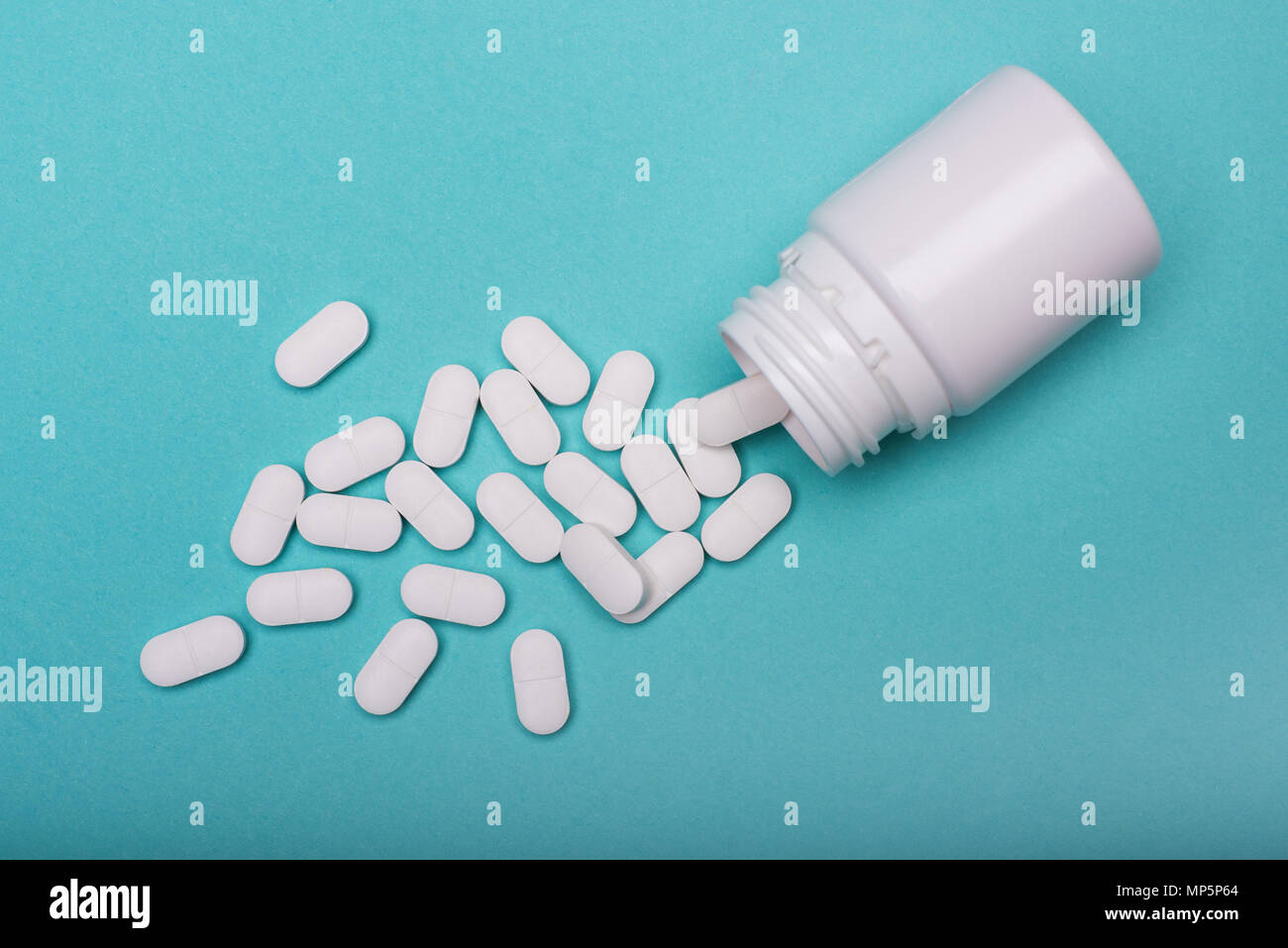 Medication bottle and white pills spilled on blue pastel coloured background. Medication and prescription pills flat lay background. Opioid epidemic. Stock Photo