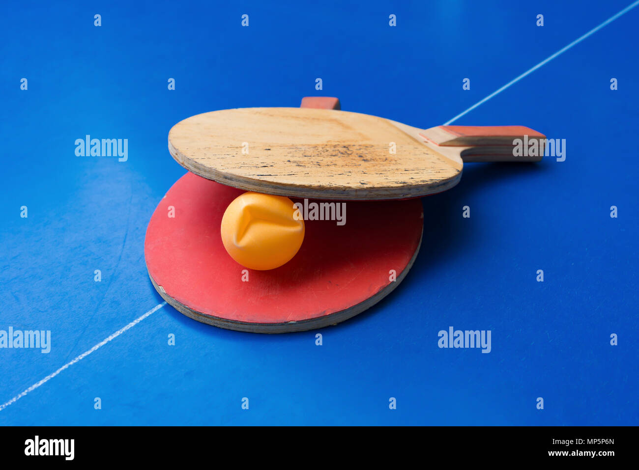 old pingpong rackets and a dented ball on a blue pingpong table Stock Photo