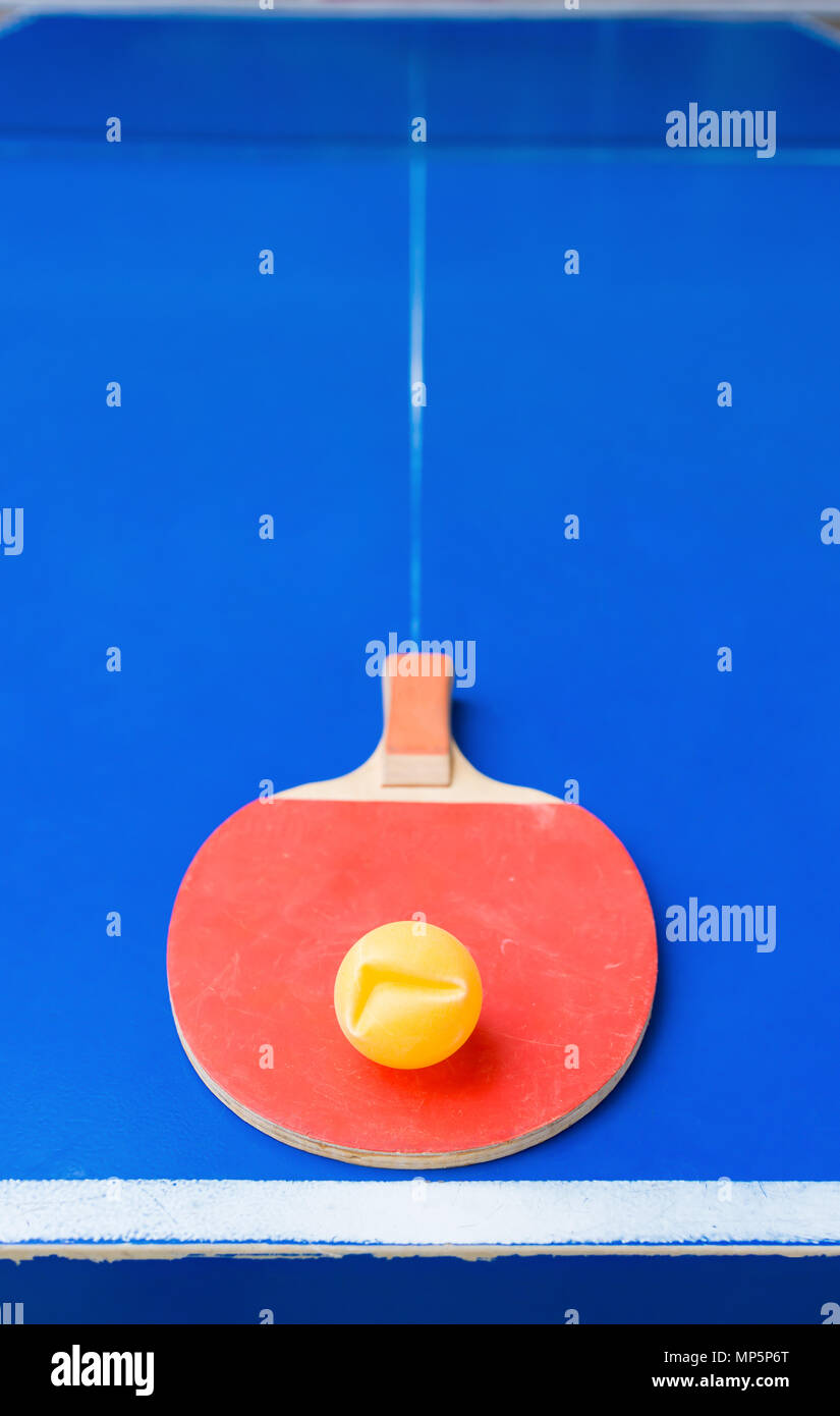 old pingpong racket and a dented ball on a blue pingpong table Stock Photo