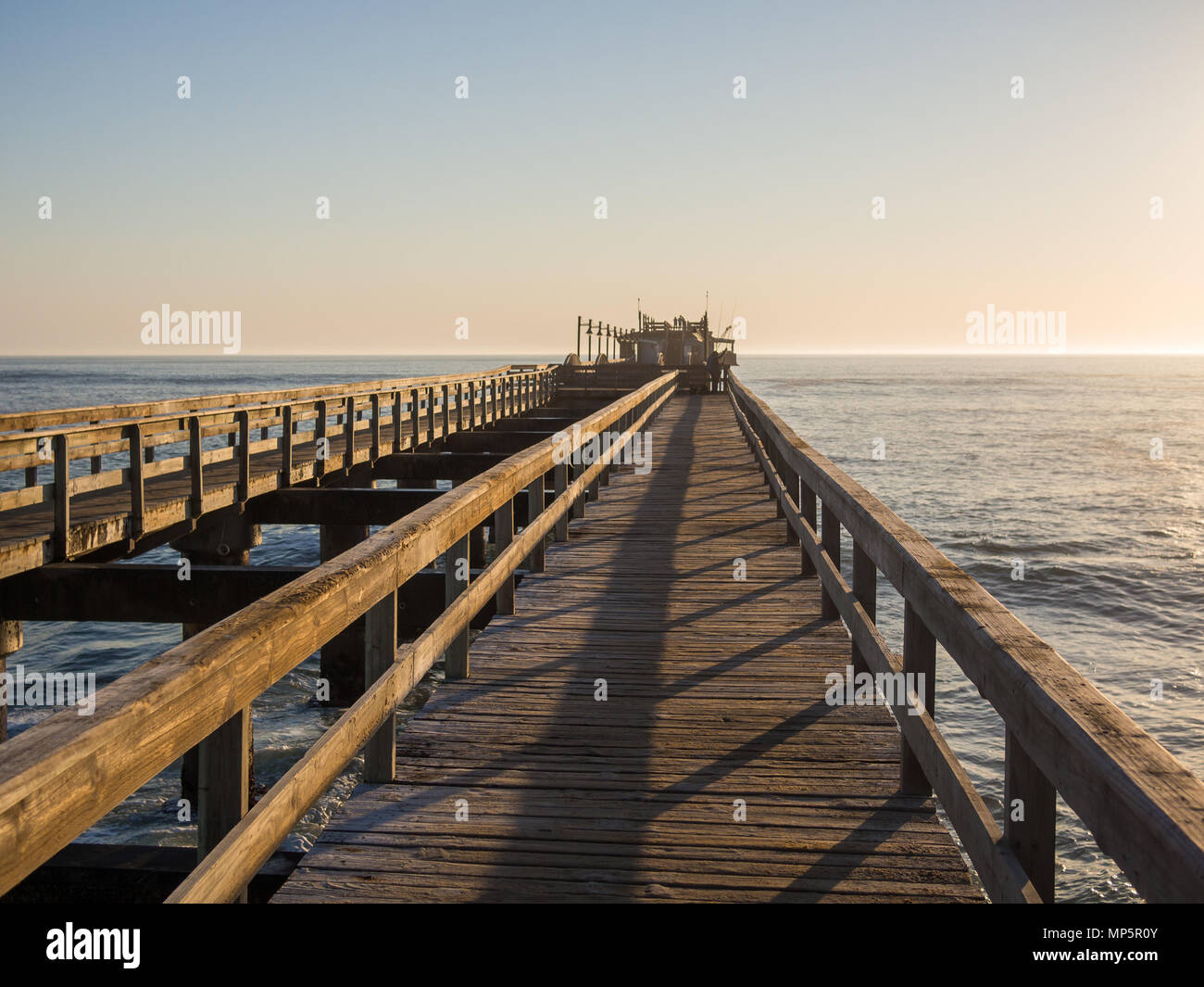 Wooden pier leading out into ocean with calm sea during soft sunset, Swakopmund, Namibia Stock Photo