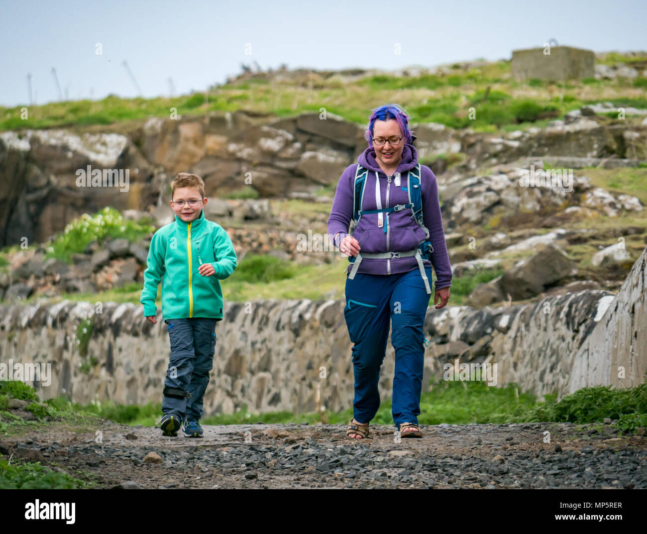 Woman with coloured hair and smiling young boy with glasses and leg brace walking on Isle of May, , Scotland, UK Stock Photo