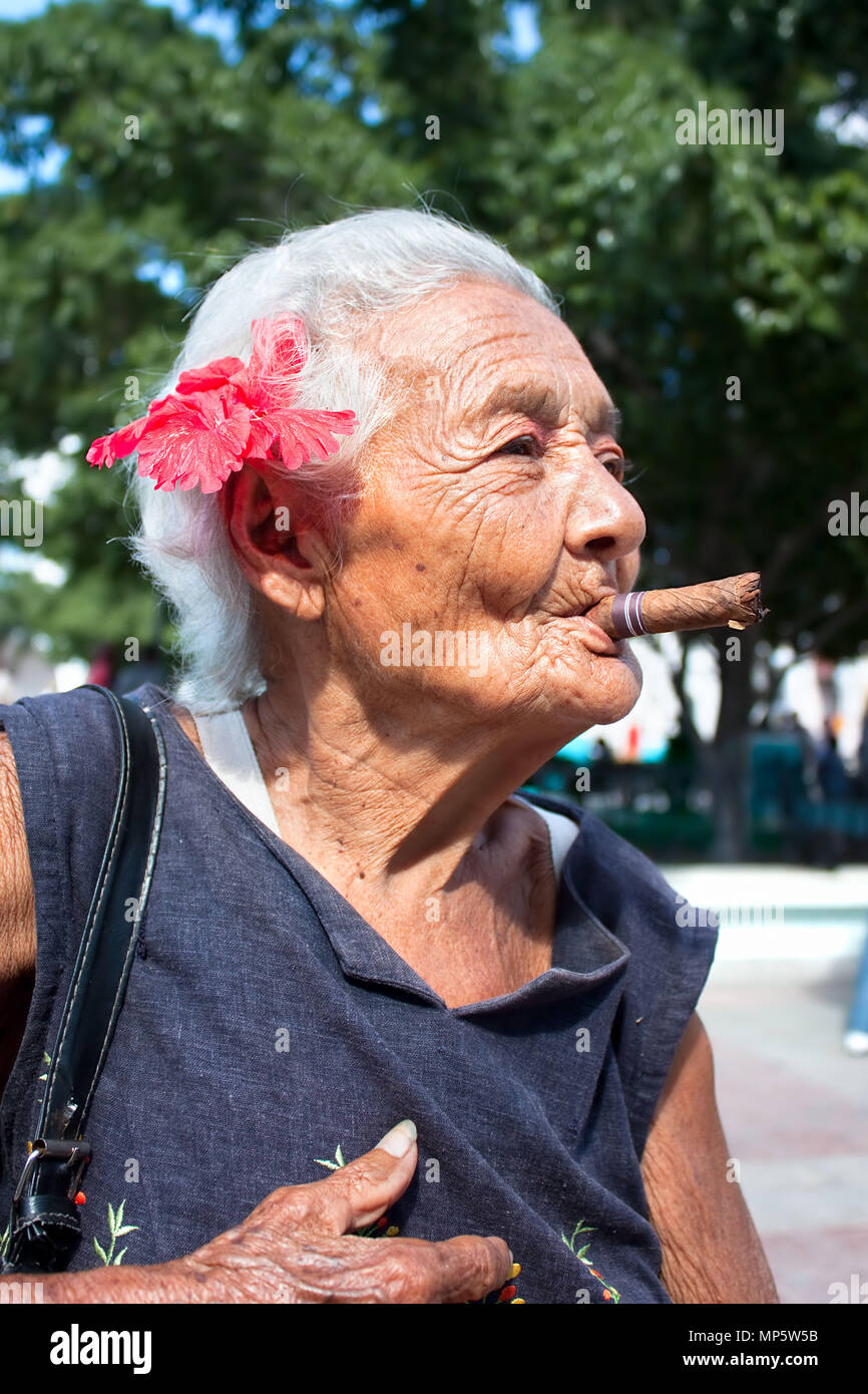 cigarette grandma summer Old wrinkled woman with red flower smoking cigar. Santiago de Cuba, Cuba  Stock Photo