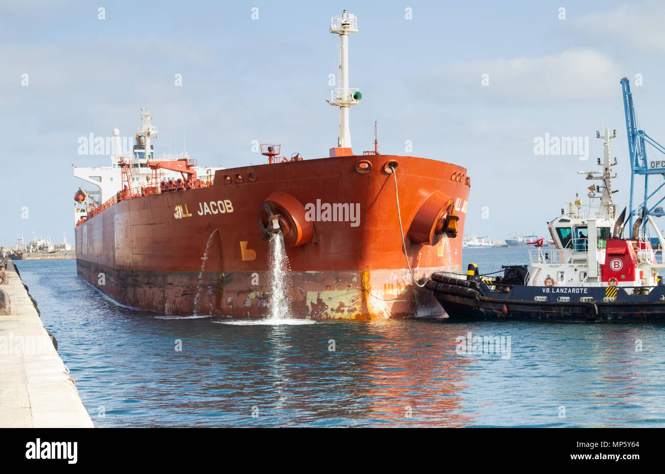 Oil tanker pumping ballast water as tug boat guides ship onto berth in port Stock Photo