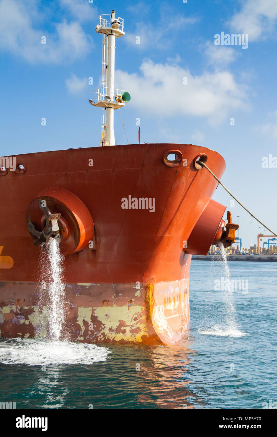 Oil tanker pumping ballast water as tug boat guides ship onto berth in port Stock Photo