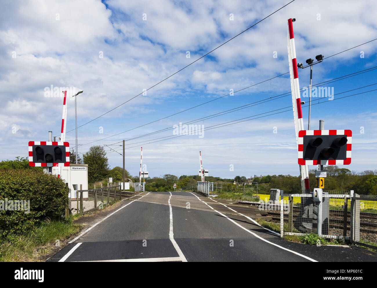 Level crossing with raised barrier over railway lines at Warkworth, Northumberland, UK which services passenger and freight trains. Stock Photo