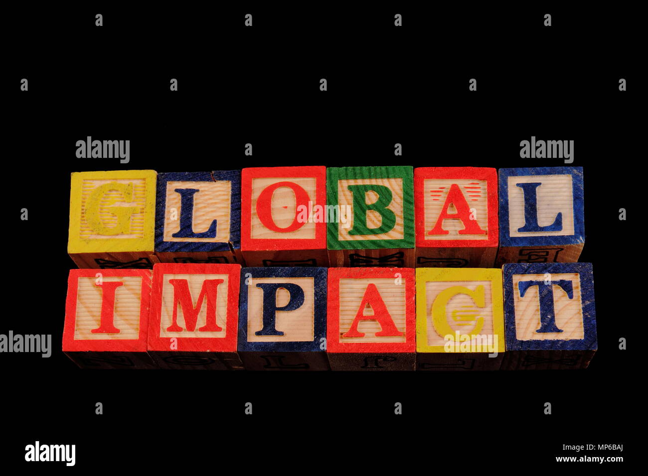 The term global impact visually displayed on a black background using colorful wooden toy blocks image with copy space in landscape format Stock Photo