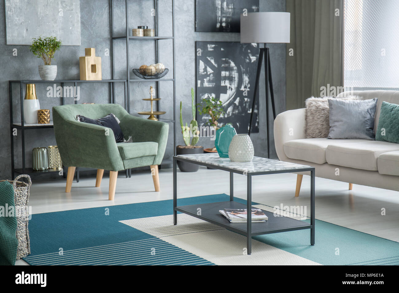 Table between green armchair and settee in modern living room interior with black paintings Stock Photo