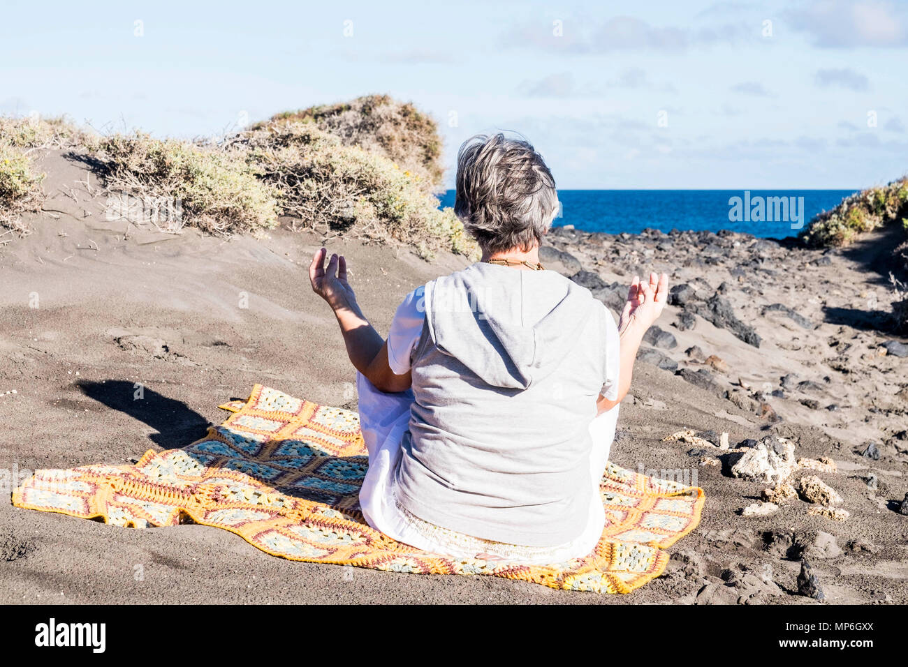 Daily meditation yofa concept for adult woman 70 years old on the beach near the power of the ocean, natural energy from the earth and water elements. Stock Photo
