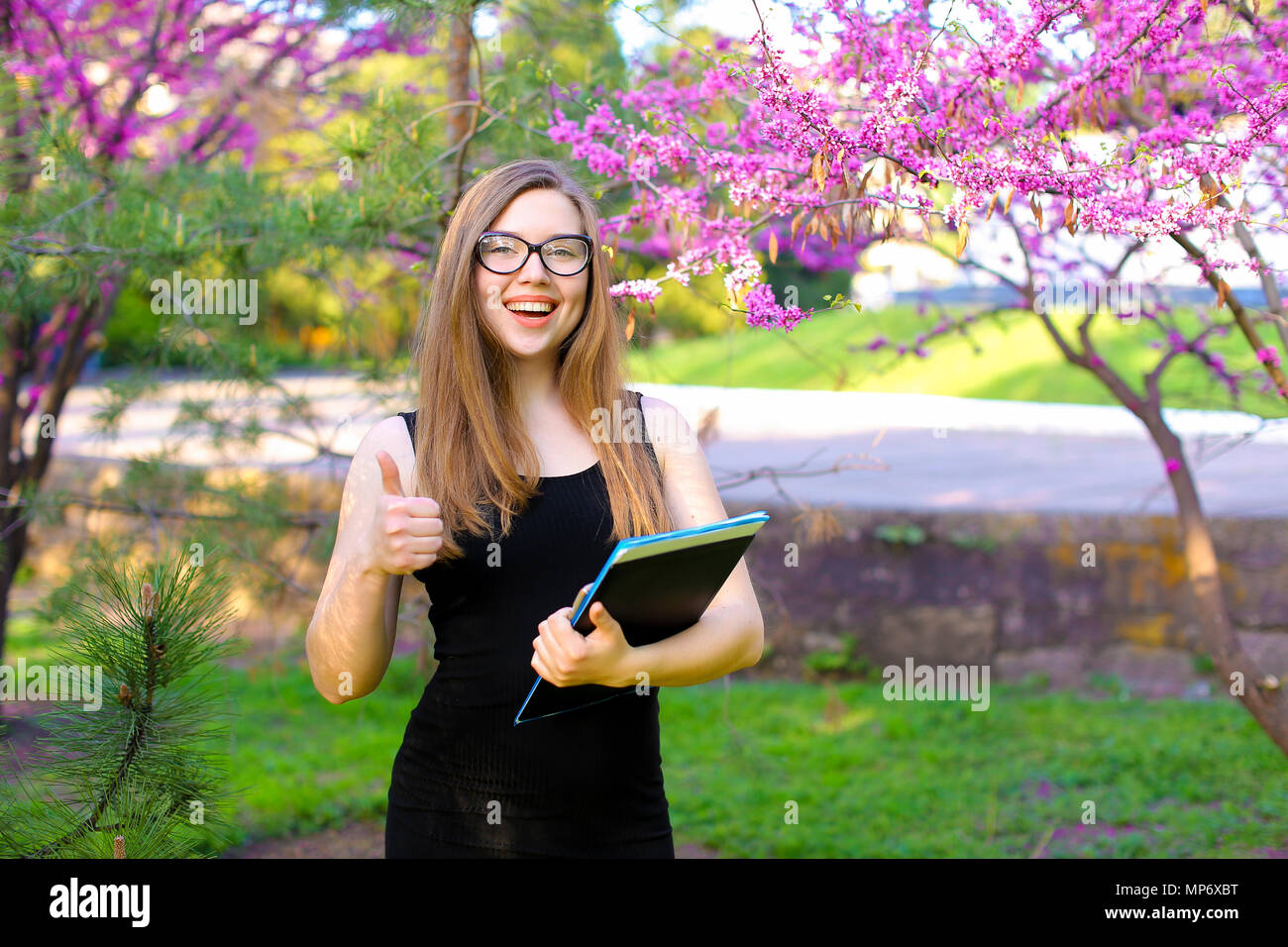 Female student showing thumbs up in garden with documents in black ...
