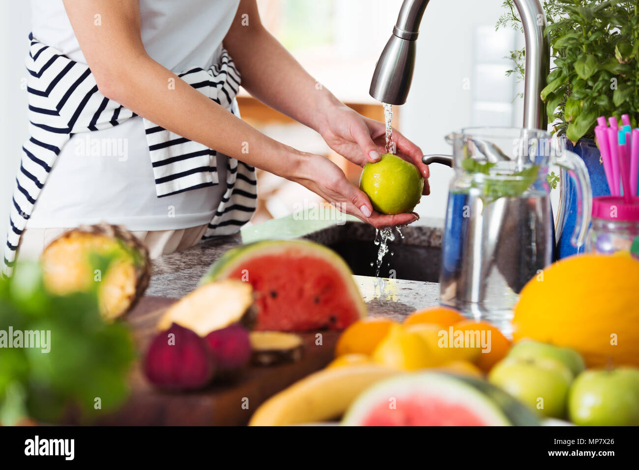 Healthy woman washing an apple above kitchen sink while preparing fresh breakfast with fruit Stock Photo