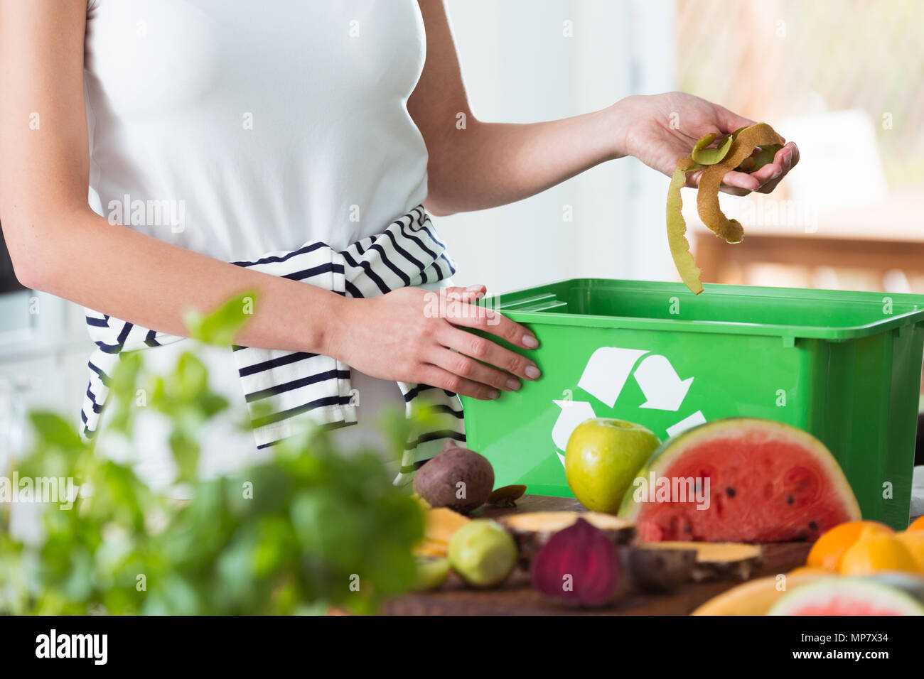Woman recycling organic kitchen waste by composting in green container