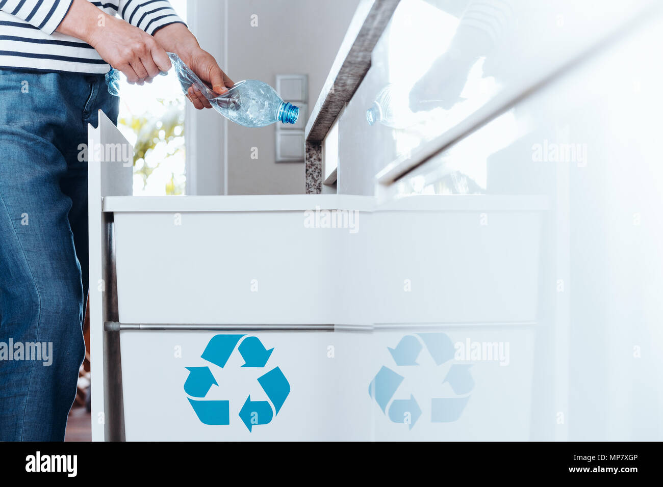 Smart person sorting waste in modern kitchen with special bin with blue symbol for plastic packaging Stock Photo