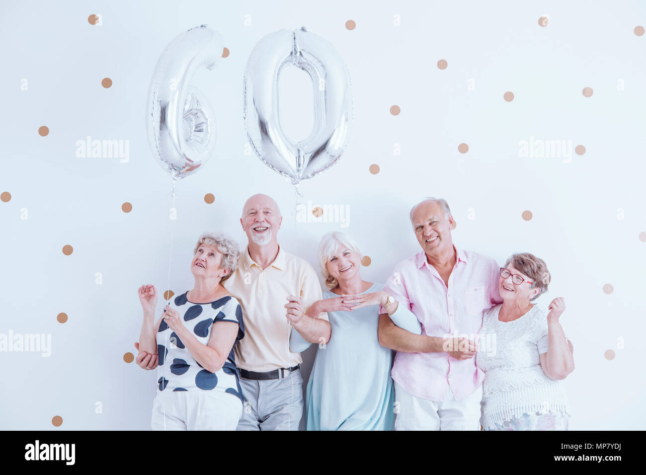 Enthusiastic seniors celebrating elderly woman's birthday with silver balloons Stock Photo