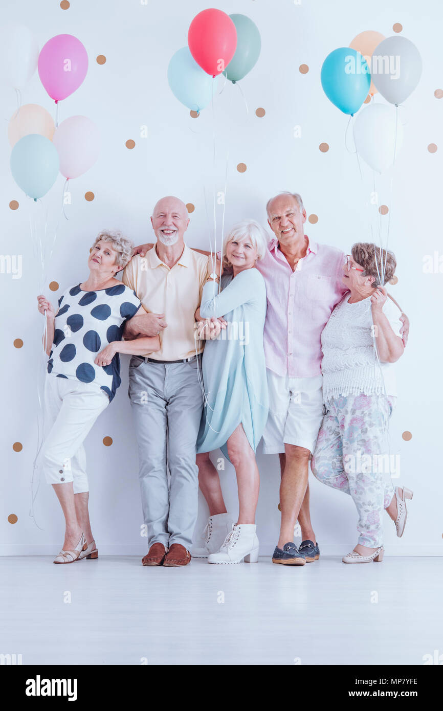 Group of enthusiastic senior friends with colorful balloons celebrating birthday Stock Photo