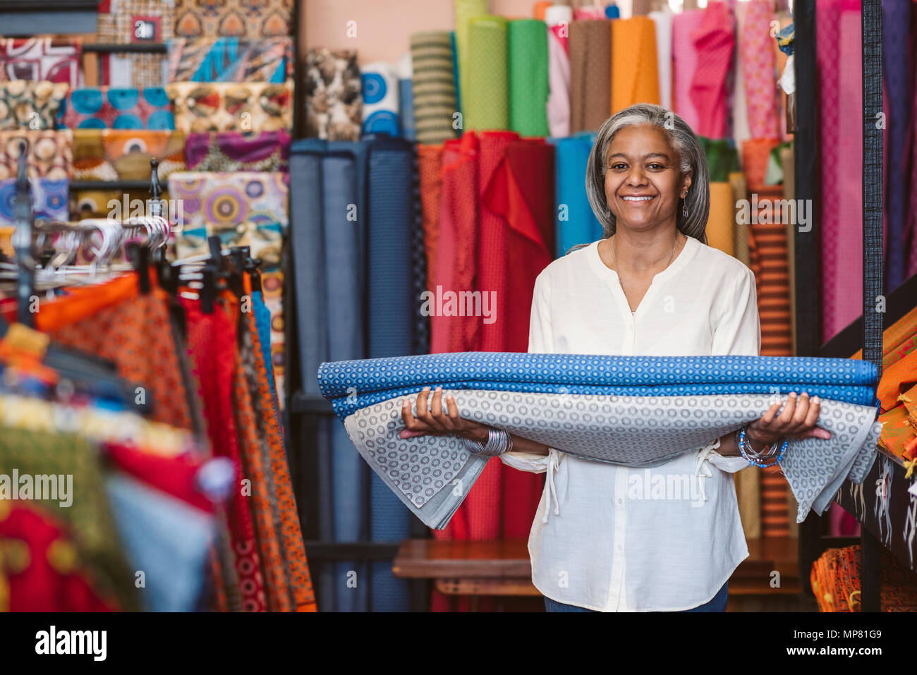 Smiling mature woman holding cloth rolls in her fabric shop    Stock Photo