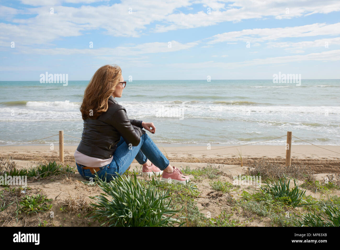 Rear view shot of relaxed middle aged woman sitting on beach and ...