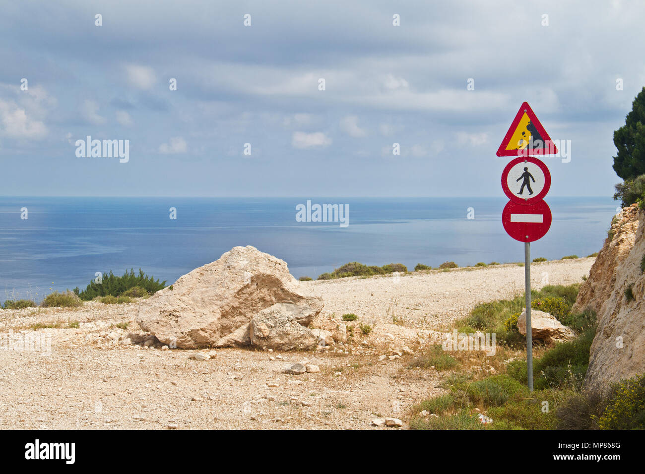 A road with a beautiful view on the Ionic sea, blocked by a fallen rock, several traffic signs warning and forbidding to use the road Stock Photo