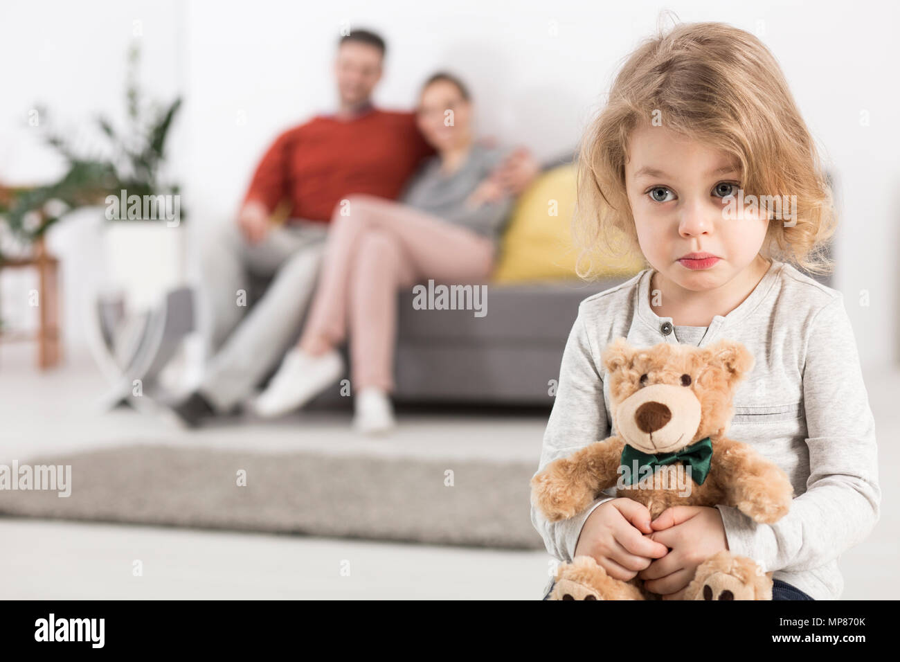 Cute Girl With Teddy Bear In The Background Man And Woman Sitting On Sofa Stock Photo Alamy