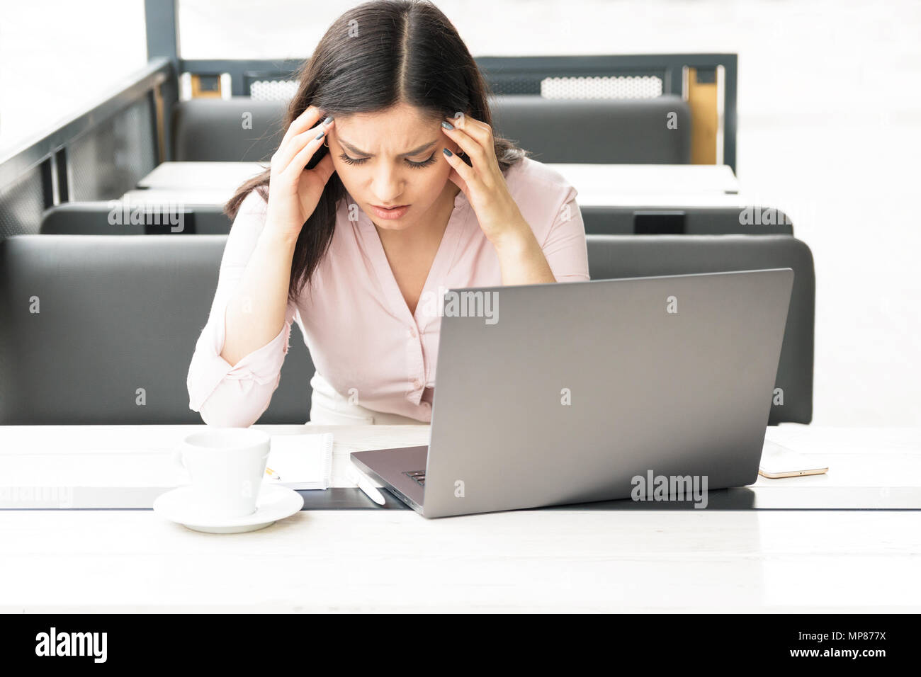 A tired woman holding her head in front of her laptop, having headache and being exhausted of work. Stock Photo