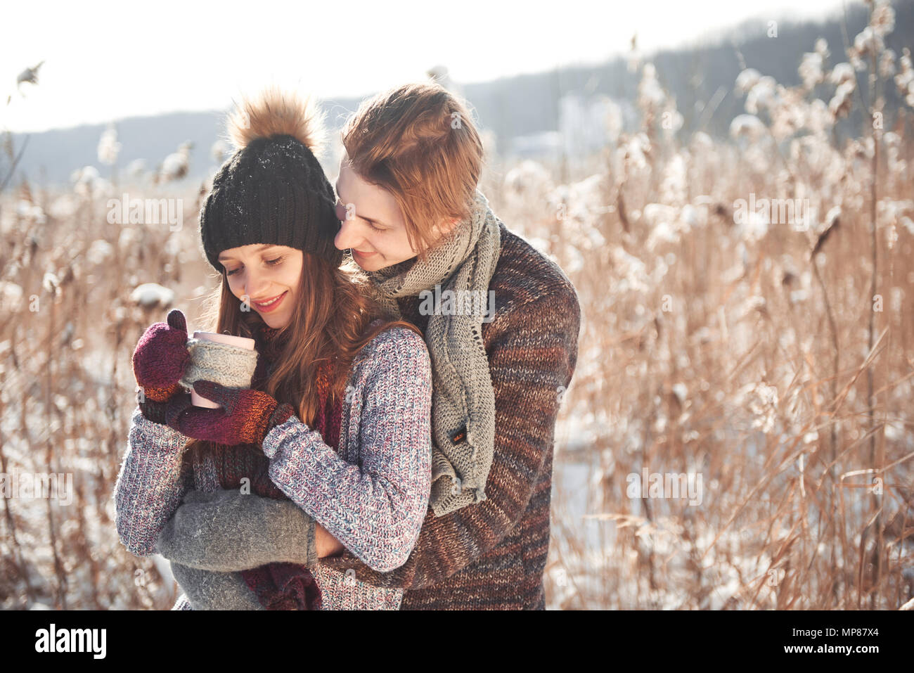 Photo of happy man and pretty woman with cups outdoor in winter. Winter holiday and vacation. Christmas couple of happy man and woman drink hot wine. Couple in love Stock Photo