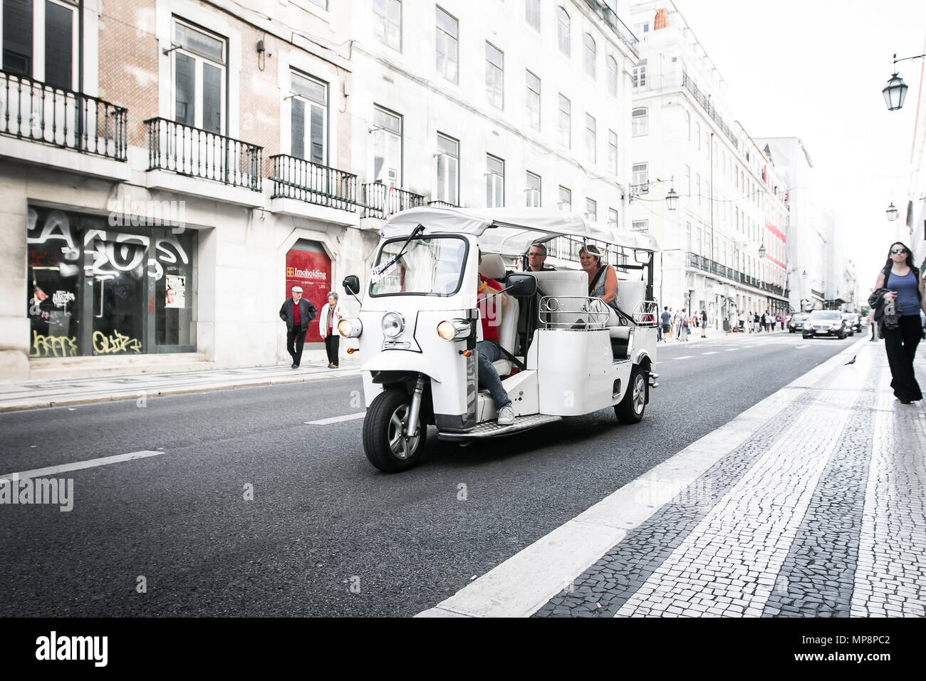 Lisbon, Portugal, May 5, 2018: Tourists are traveling by a traditional tuk-tuk vehicle down a street in downtown Lisbon. Stock Photo