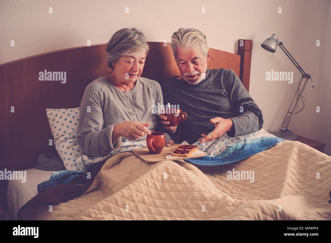 caucasian aged couple doing breakfast at home in the bed. nice natural scene at home for togheterness life concept. love and carefree people married. Stock Photo