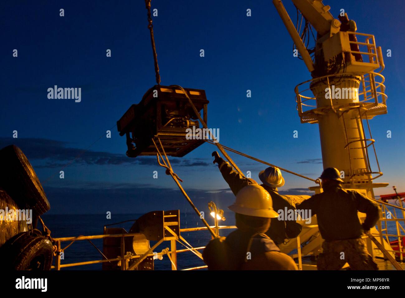 U.S. Navy sailors deploy an underwater remotely operated vehicle (ROV) from the deck of the Norwegian offshore construction support vessel Skandi Patagonia at night December 1, 2017 in the Atlantic Ocean.   (photo by Derek Harkins via Planetpix) Stock Photo