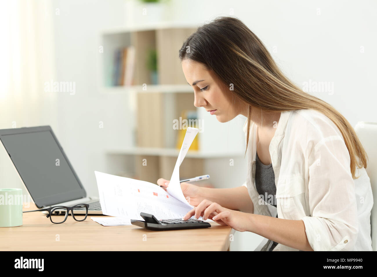 Side view portrait of a woman calculating expenses on a desktop at home Stock Photo