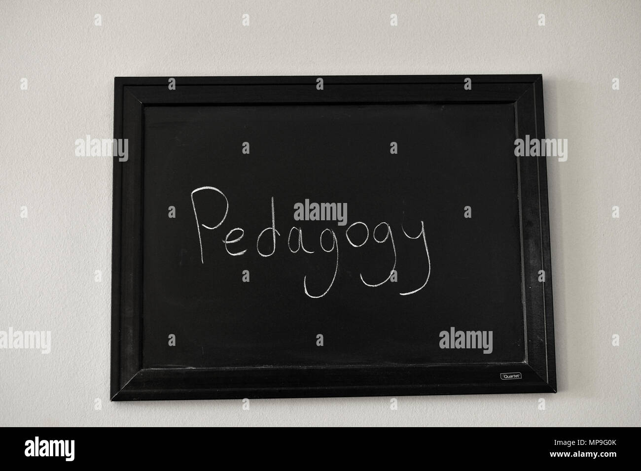 Pedagogy written in white chalk on a wall mounted blackboard. Stock Photo