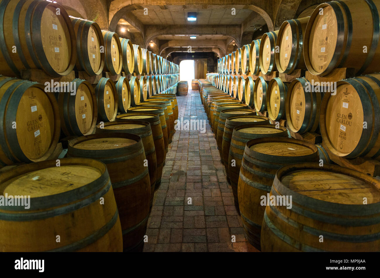 Wine aging in oak wooden casks in the cellar of a winery with vineyard, located between Stellenbosch and Cape Town, South Africa. Stock Photo