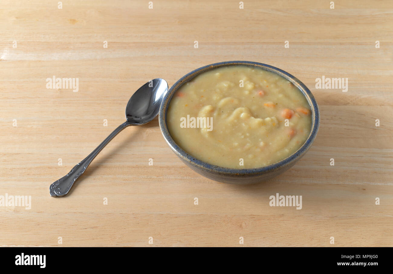 A bowl of home style potato soup in a stoneware bowl with a spoon to the side atop a wood table top. Stock Photo