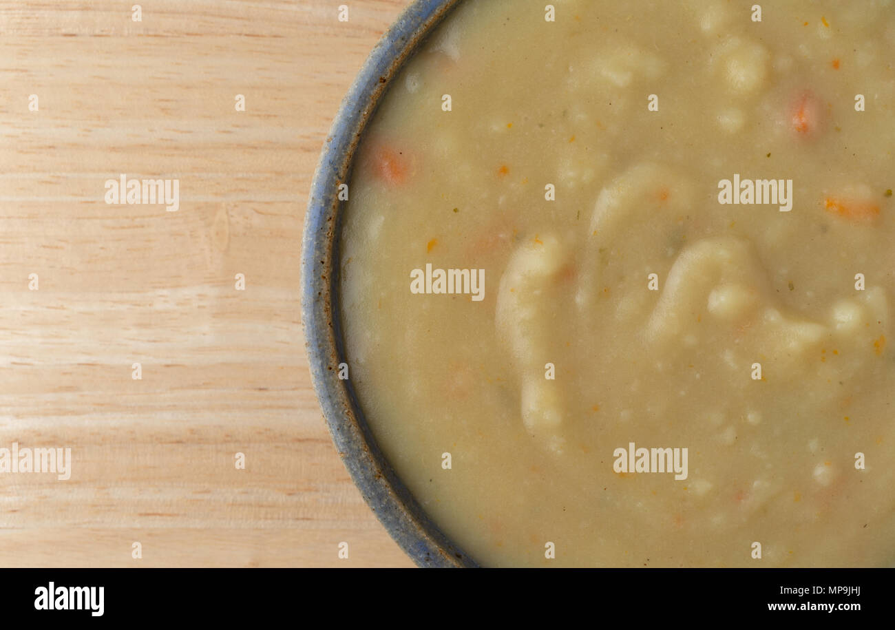Top close view of a bowl of home style potato soup in a stoneware bowl atop a wood table top. Stock Photo