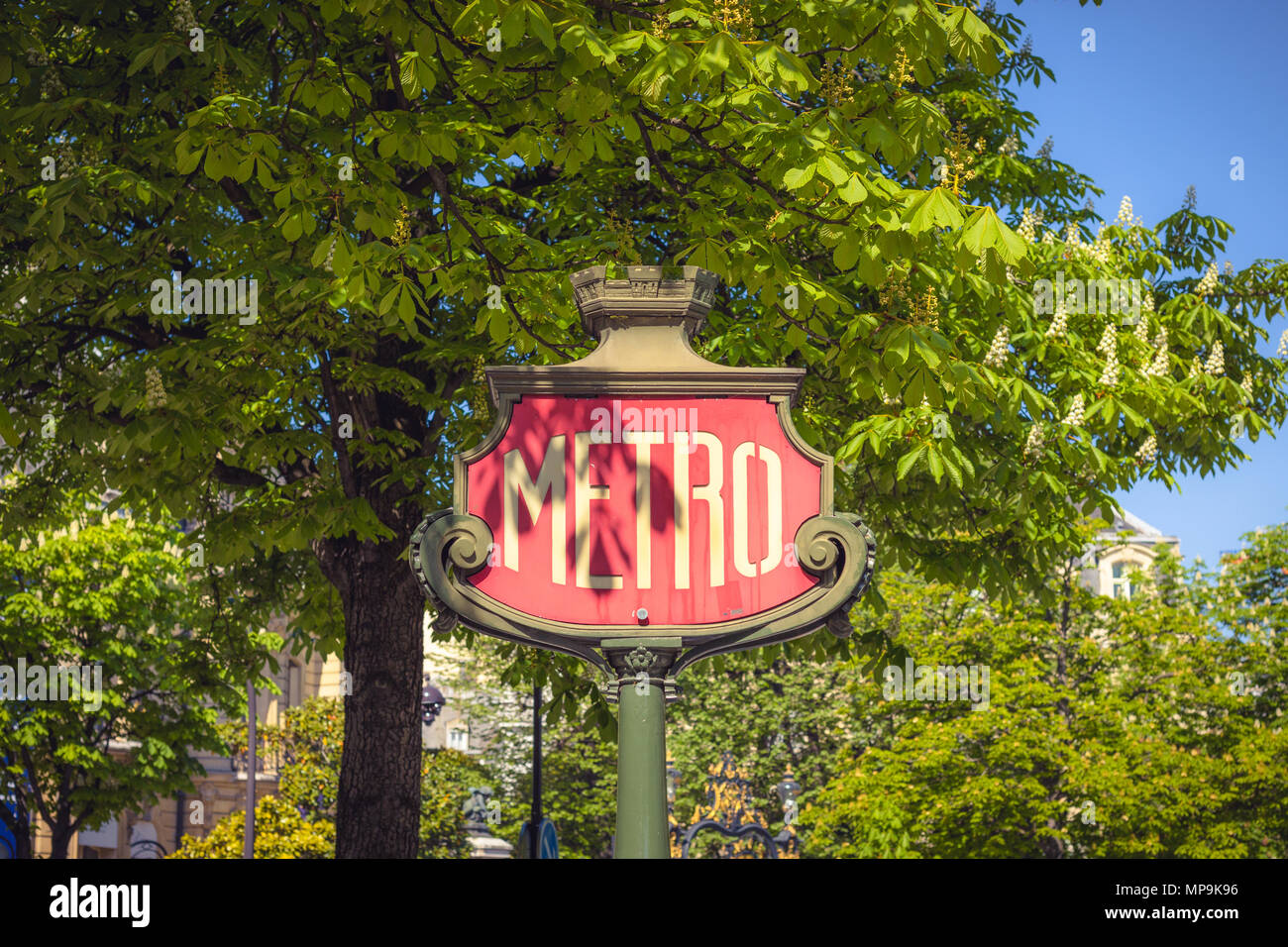 old vintage metro sign surrounded by trees in a street of Paris during a sunny day of spring . Stock Photo