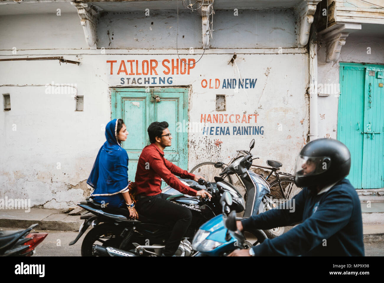 a man and a couple on motorcycles passing a tailor shop in Udaipur, India Stock Photo