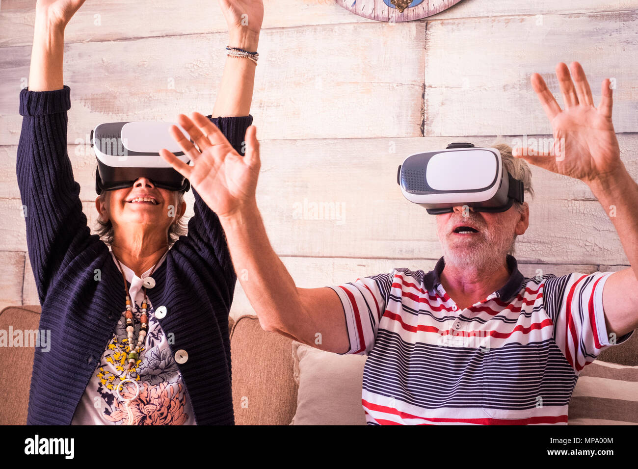 aged senior man and woman playing with goggles headset at home sit down on the sofa. roller coaster feeling Stock Photo