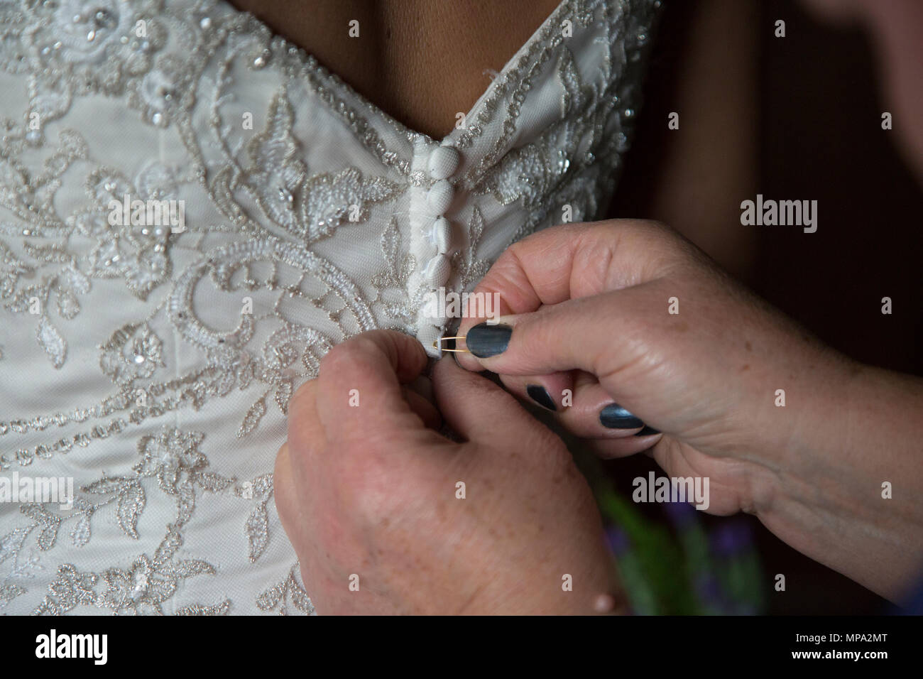 Brides dress being done up by her mother on her wedding day, close up of the buttons on the back of the wedding dress Stock Photo