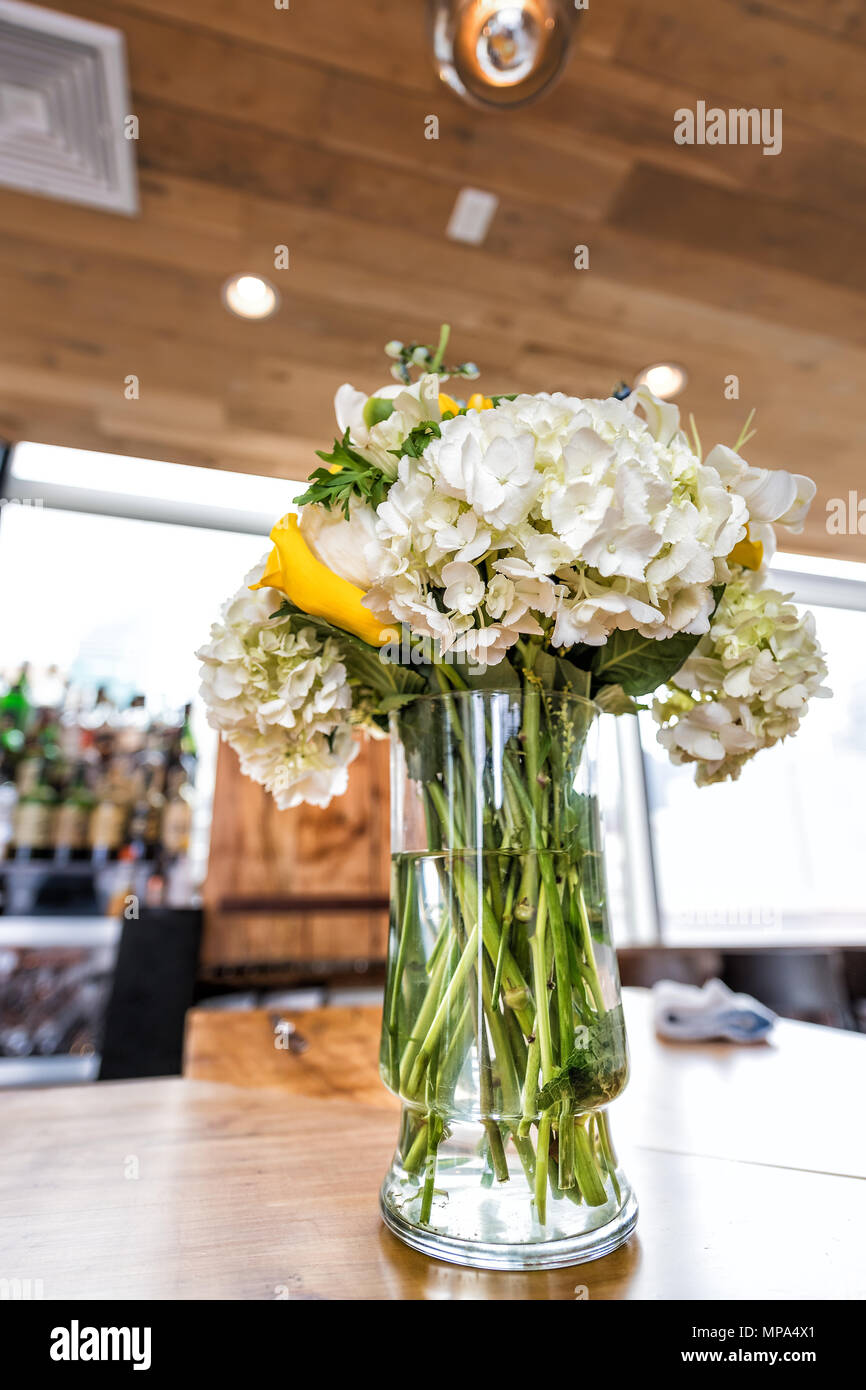 Closeup of one wedding flower bouquet arrangement on wooden table of reception dinner in restaurant venue, alcohol bar background Stock Photo